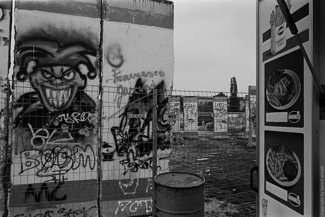 Dokumentarfotografie - Narr auf Berliner Mauer neben einer Imbisbude - Stadtportrait